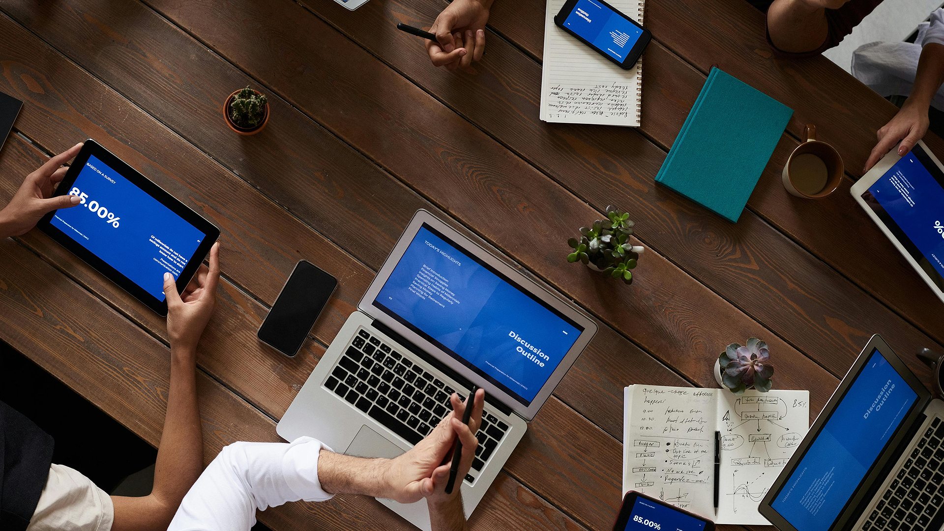 A team working together around a table with laptops and blue-screen dashboards