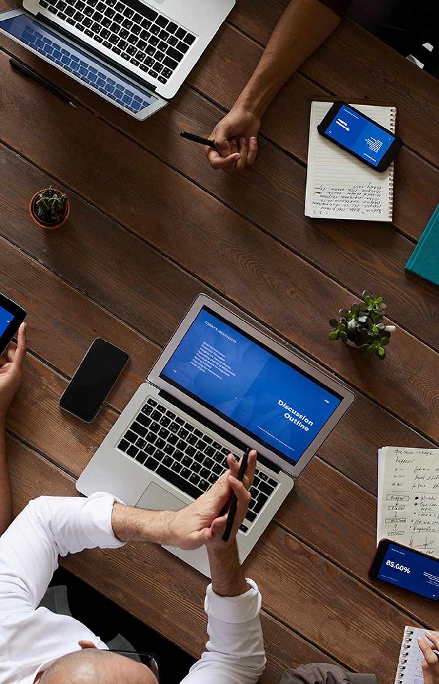 A team meeting seen from above with laptops and tablets on a wooden table